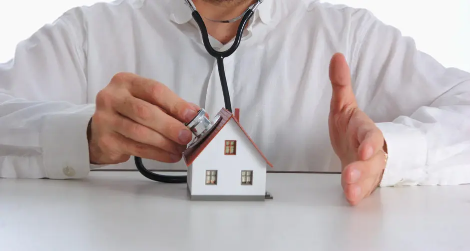 A home inspector holding a stethoscope to a small model house
